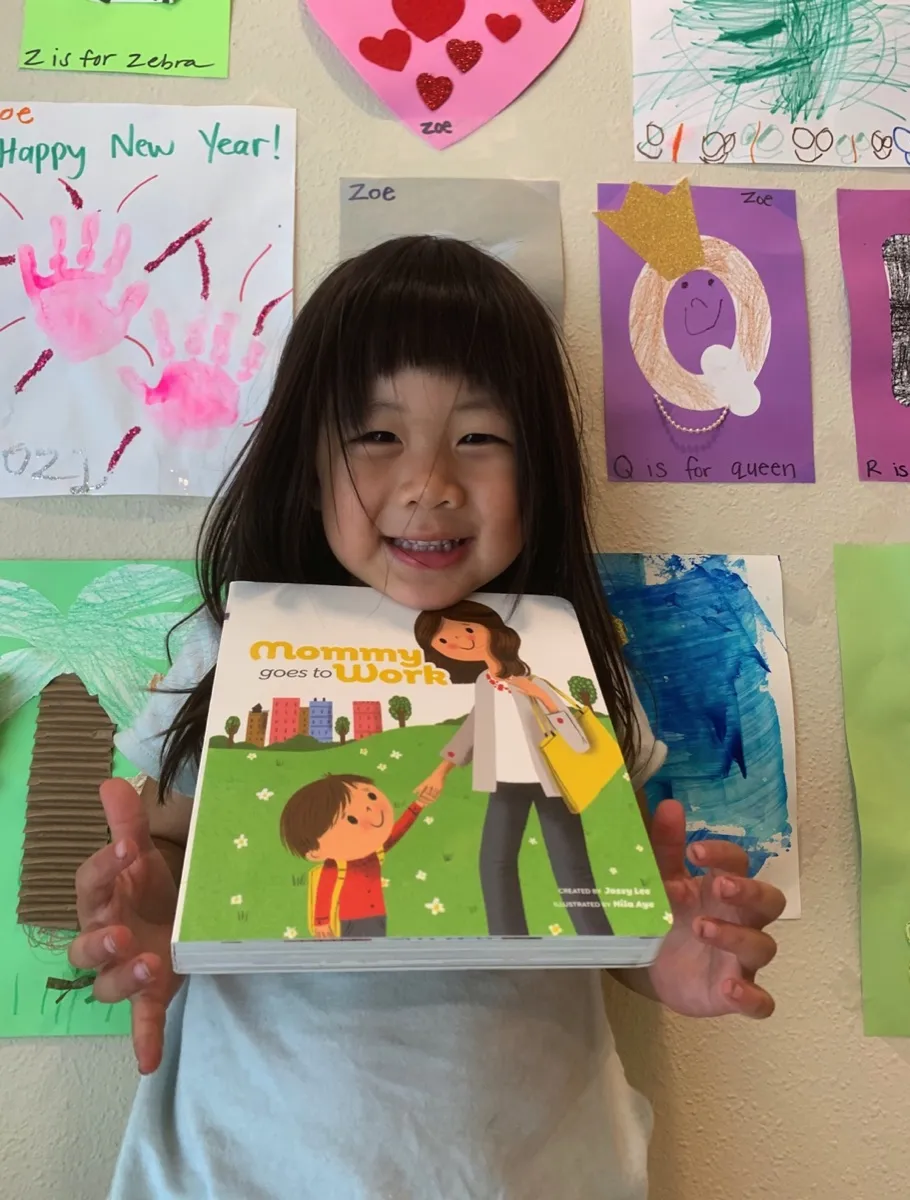 A girl holding the book in front of her classroom artwork